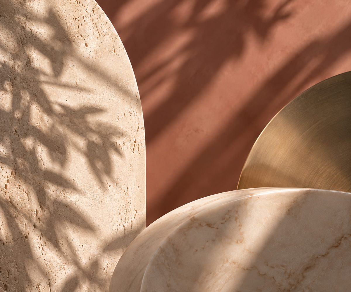 Art direction study: a pale stone arch and a brushed brass disc against a terracotta wall in raking light